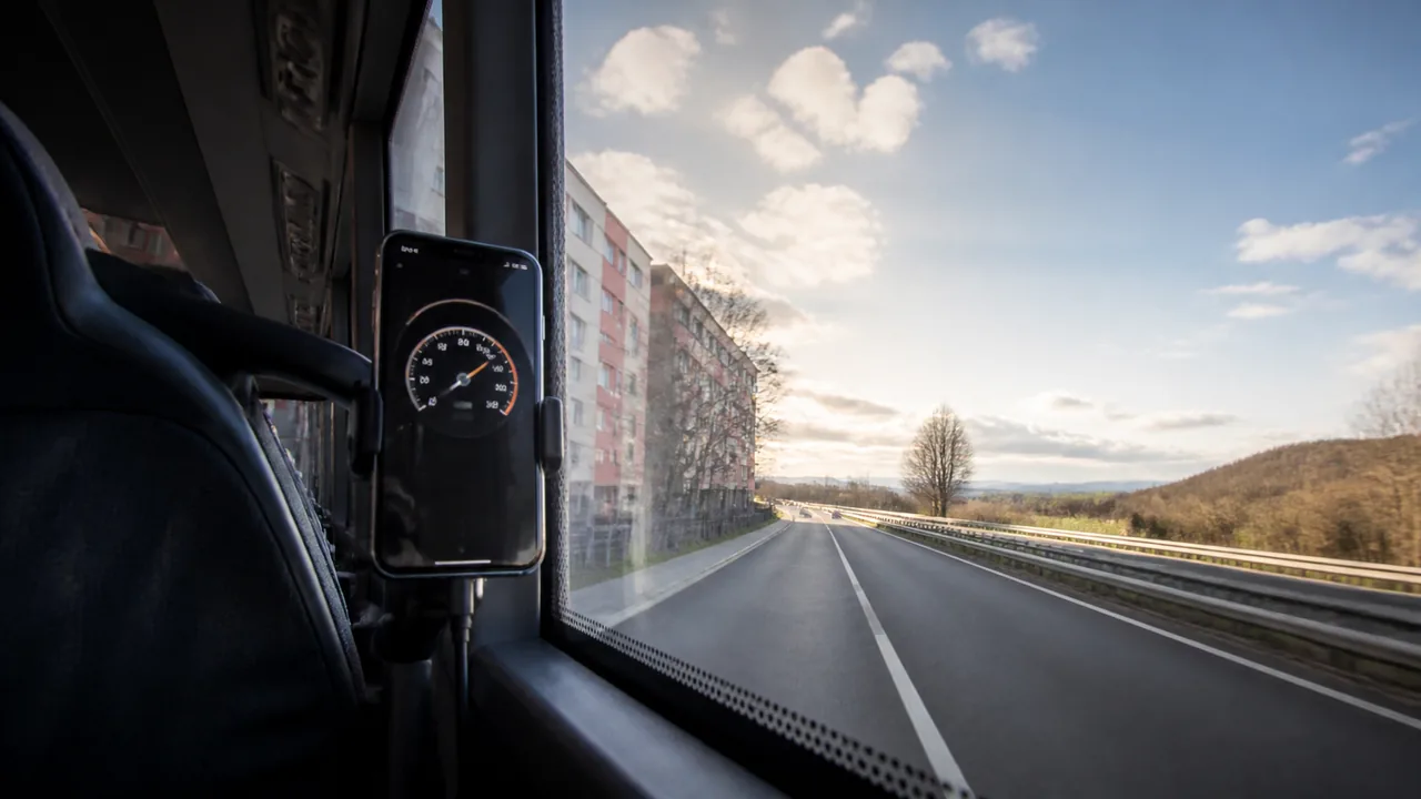 Illustrative phone speed display by a bus passenger window between urban and open-road scenery